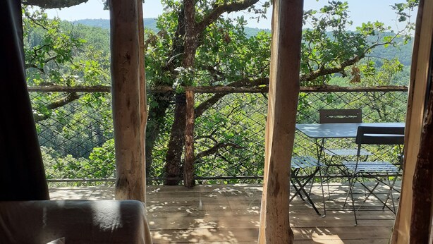 A wooden-framed window with a view of a deck and outdoor furniture. - Wooden tree house (Salvagnac-Cajarc)