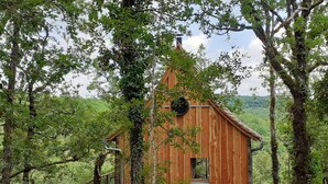 A wooden treehouse with a small window and a metal roof, surrounded by dense forest. - Wooden tree house (Salvagnac-Cajarc)