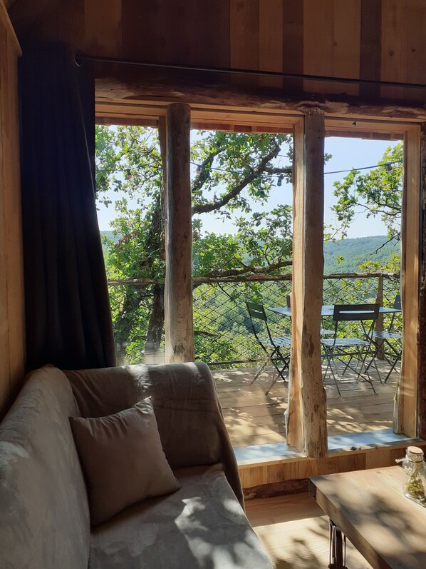 Un intérieur en bois avec un canapé et une table, de grandes fenêtres donnant sur un espace extérieur aménagé et sur la verdure.