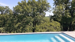 A swimming pool with a wooden deck, surrounded by lush green trees and hills in the background. - Wooden tree house (Salvagnac-Cajarc)
