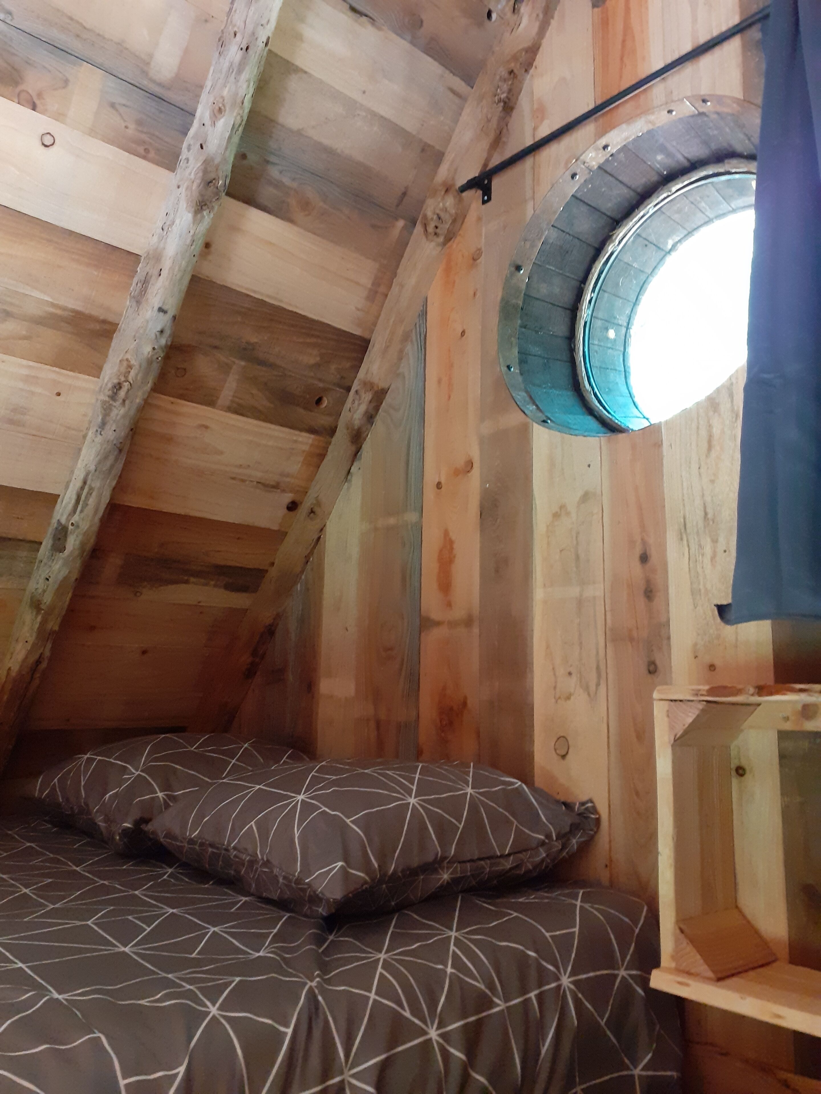 Een houten interieur met een schuine kap, een rond dakraam en een bed met beddengoed met een patroon.