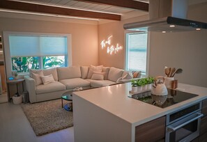 Relax in a cozy boutique hotel atmosphere with a spacious living area featuring a central kitchen island, comfortable sofa, and large windows.