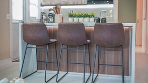 A modern kitchen with wooden cabinets, a central island with bar stools, and a dining area with a round table and chairs.