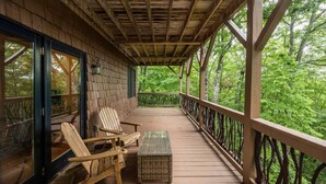 A wooden deck with two Adirondack chairs and a small table, overlooking a lush green forest. - Nature lovers paradise in Connestee Falls 14 minutes to Brevard! (Brevard)