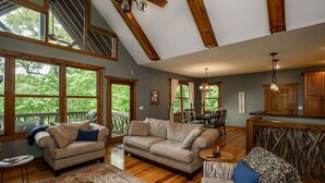 A spacious living room with a high ceiling, large windows, and a cozy seating area. - Nature lovers paradise in Connestee Falls 14 minutes to Brevard! (Brevard)