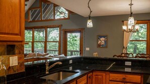A kitchen with a granite countertop, wooden cabinets, a sink, and a chandelier. - Nature lovers paradise in Connestee Falls 14 minutes to Brevard! (Brevard)