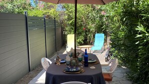 An outdoor patio with a table set for dining, surrounded by chairs, under a large umbrella.