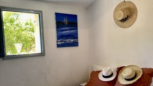 A bedroom with a bed, two pillows, a window, a painting, and a hat on the wall.