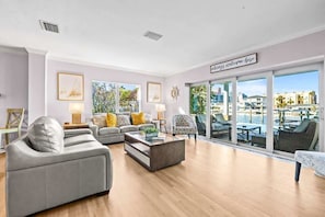 A modern living room with a sofa, armchair, and coffee table, large windows with a city view, and a sign reading 'always welcome here.'