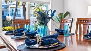 Une table à manger dressée avec des serviettes, des assiettes et des couverts bleus, et offrant une vue sur les bâtiments et les palmiers à l’extérieur.