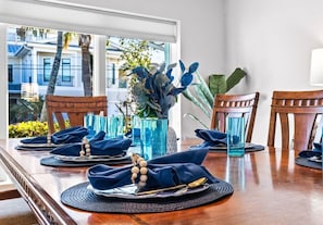 A dining table set with blue napkins, plates, and cutlery, with a view of buildings and palm trees outside.