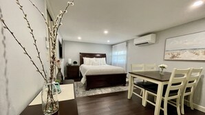 A bedroom with a bed, bedside table, and a nightstand. There is a dining area with a table and chairs.