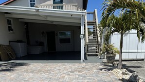 A covered parking area with a paved walkway, a building entrance, and a palm tree.