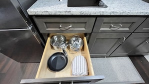 A kitchen with a granite countertop, a stainless steel refrigerator, and a drawer with pots, pans, and a striped cloth.