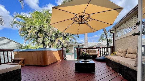 A wooden deck with a hot tub, outdoor seating, and a large umbrella.
