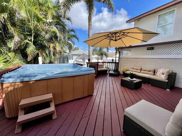 Relax on the deck with a hot tub, wicker sofa, and lush greenery surrounding you.