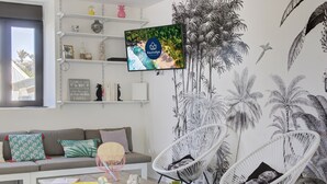 A living room with a sofa, two white wicker chairs, a coffee table, and a TV mounted on the wall displaying a KeyLodge advertisement. - Villa Raj Mahal, 2 minutes from the beach (Saint Paul)
