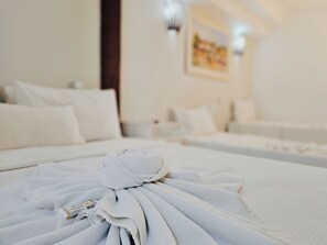 A neatly made bed with a folded towel and a small tag, a white sofa, and a painting on the wall in a hotel room. - Pousada Ilha Branca Centro (Búzios)