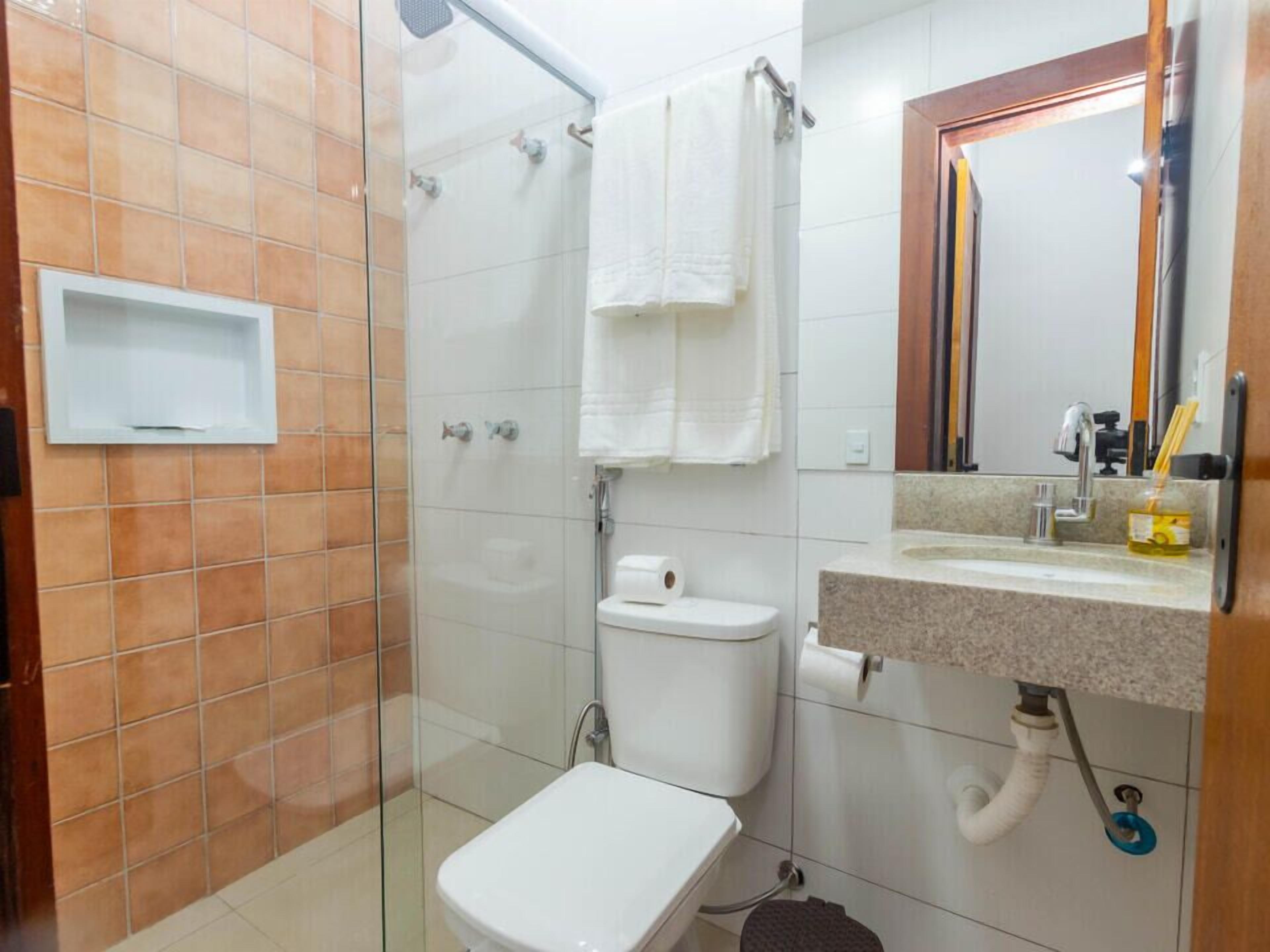 Een badkamer met een douchecabine van glas, een toilet, een wastafel met spiegel en een handdoekrek.