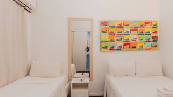 Habitación de hotel con dos camas individuales, una mesita de noche con lámpara, un espejo y una obra de arte colorida en la pared.