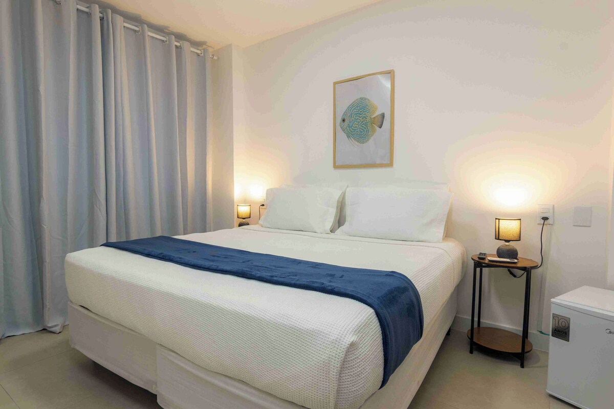 A hotel room with a bed, two bedside lamps, a small table, a nightstand, and a wall-mounted picture.