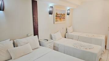 A hotel room with two beds, each with white linens and a decorative towel. There are wall-mounted lights and a painting above the beds.