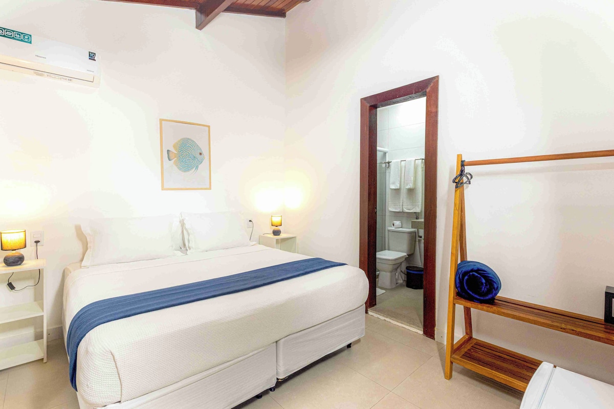 A hotel room with a bed, bedside lamps, a wooden shelf, and a bathroom visible through an open door.