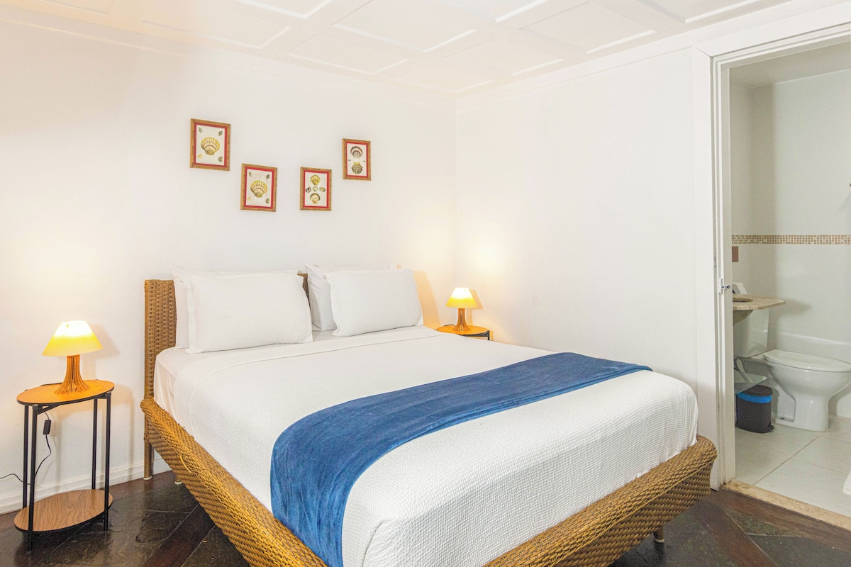 A hotel room with a bed, two bedside lamps, a blue throw blanket, and framed pictures on the wall.