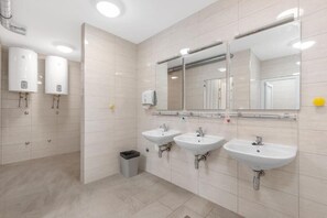 Un baño moderno con tres lavamanos, un espejo grande y dos calentadores fijados a la pared.