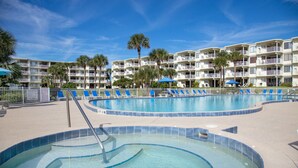 A hotel pool area with multiple levels of balconies, a hot tub, and lounge chairs.