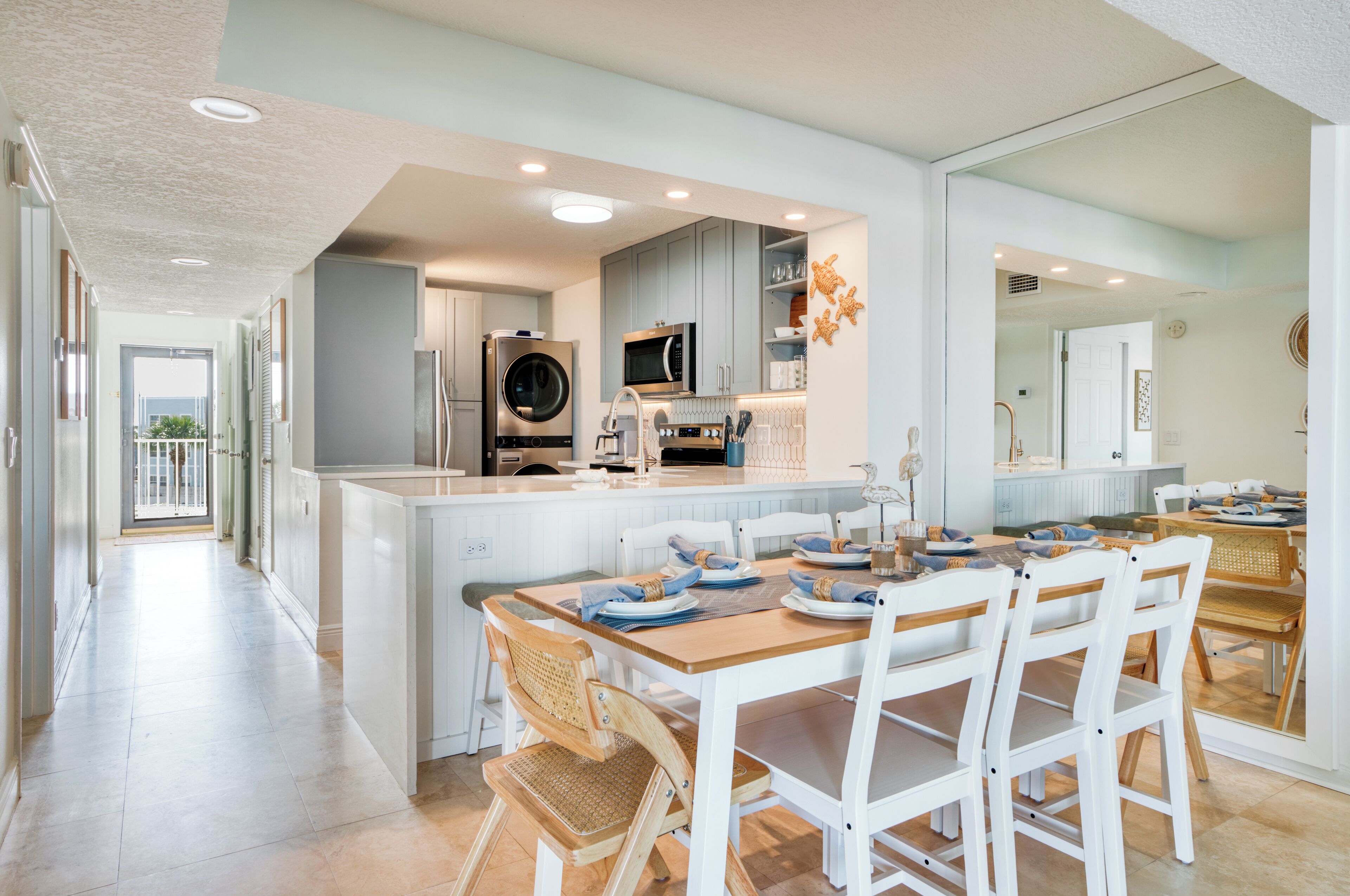 A modern kitchen with a central island, white cabinetry, and a dining area with wooden chairs.