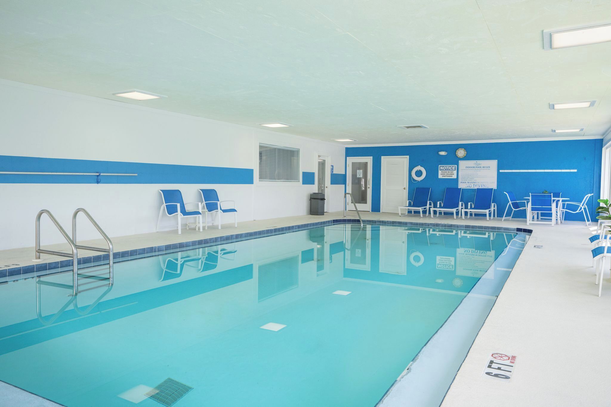 En inomhuspool med kristallklart blått vatten, omgiven av blå och vita väggar, och utrustad med flera solstolar.