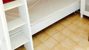 A bunk bed with a red headboard and white side panels, a small shelf above the bed, and a tiled floor.