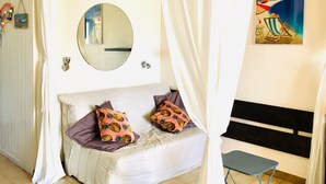 A bedroom with a bed, a bedside table, a chair, a mirror, and a painting on the wall.