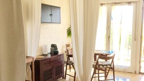 A room with a dining table, chairs, a small cabinet, and a television on the wall.