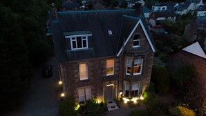 Ett tvåvåningshus med ett brant tak, många fönster och en väl upplyst trädgård framför huset.
