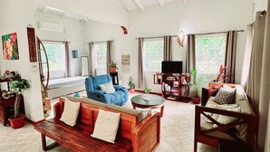 A spacious living room with a wooden sofa, a blue armchair, and a wooden coffee table. There are potted plants and a television in the room. - Maison 79 – Your Private Soufrière Escape w/ 2BR, 2BA, AC & WiFi (Soufrière)