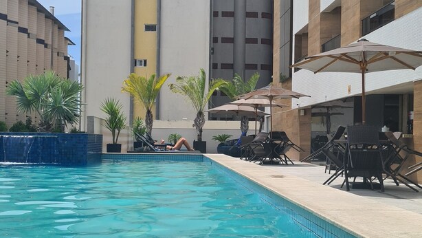 A swimming pool with lounge chairs and umbrellas, surrounded by buildings. - GOLDFLAT CABO BRANCO JOÃO PESSOA (João Pessoa)