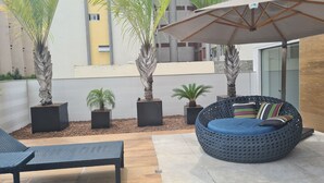 A patio area with a round blue sofa, a black woven chair, and several potted plants. - GOLDFLAT CABO BRANCO JOÃO PESSOA (João Pessoa)