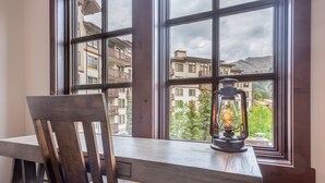A wooden desk with a chair and a lit lantern by a window overlooking a building with balconies.