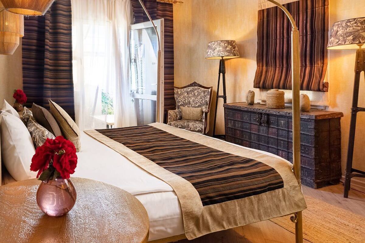 A bedroom with a large bed, a wooden floor, a round table with a vase of flowers, and a hanging light fixture.