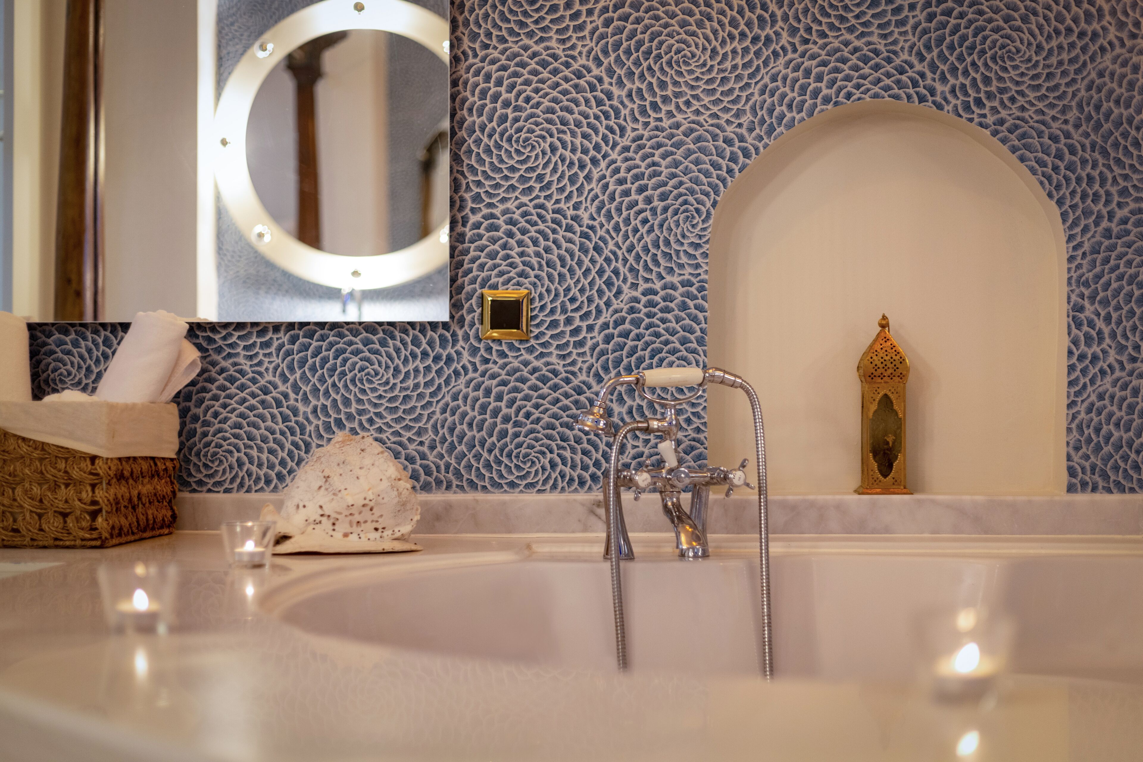 Un baño con una bañera grande, un espejo redondo con luces, una pared con textura y un adorno mural.