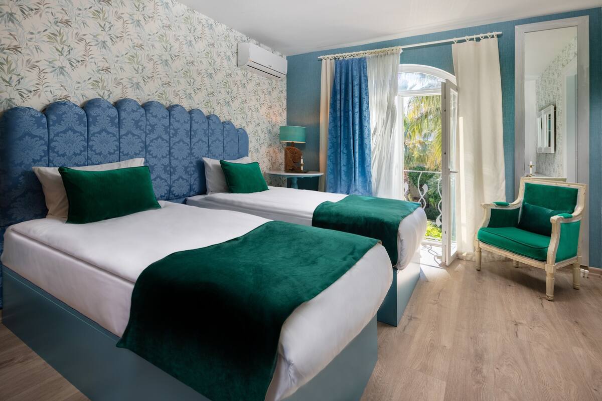 A hotel room with two beds, a chair, a small table, and a window with curtains.