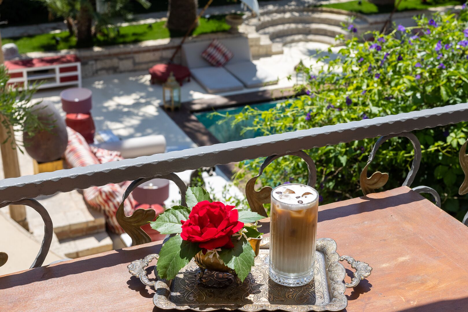 Una mesa con un vaso de café helado y una rosa roja sobre una bandeja decorativa.