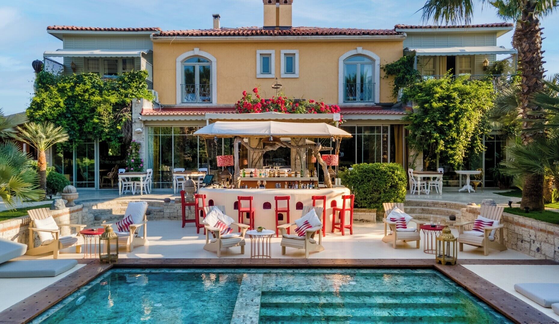 A poolside area with a bar, outdoor seating, and a large house in the background.
