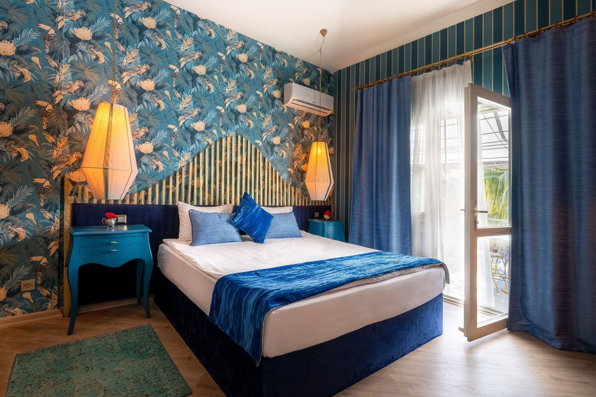 A bedroom with a bed, two nightstands, a wall-mounted air conditioner, and a view through a glass door.