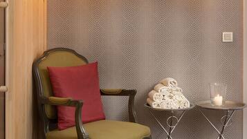 A cozy room with a patterned wall, a green armchair with a red pillow, a small table with a candle, and a woven basket.