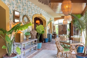 A spacious interior with a central seating area, a patterned wall, and various potted plants.
