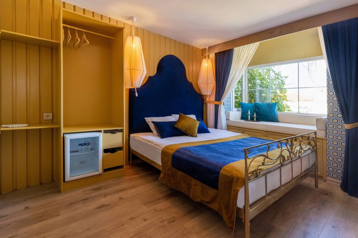 A bedroom with a bed, bedside table, wardrobe, and a window with curtains.
