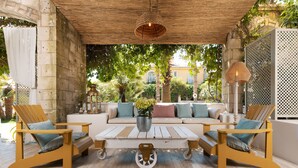 Un espacio de estar al aire libre cubierto, con dos sillas de madera, un sofá blanco y una mesa central.